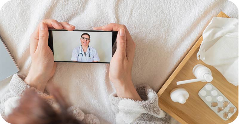 A patient using a mobile phone for a virtual doctor visit, with a tray of medical supplies and water nearby.