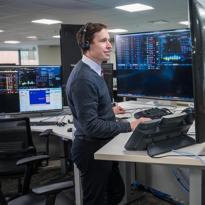 A healthcare professional wearing a headset monitors patient data on multiple large screens in a virtual ICU command center.