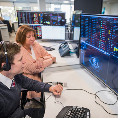 Two medical professionals in a high-tech command center analyzing patient diagnostics and digital imaging on multiple screens.