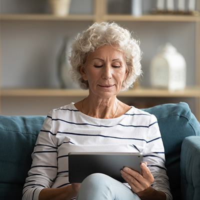 A senior woman comfortably using a tablet at home for remote patient monitoring or a telehealth consultation.