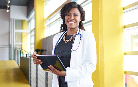 A smiling female medical provider in a white lab coat holding a tablet.